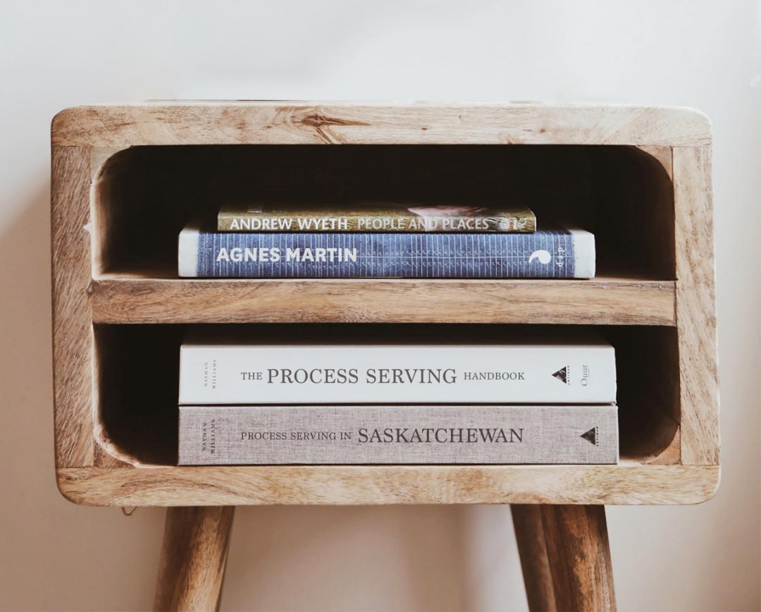 A side table made out of wood, two shelves, both holding a few books.